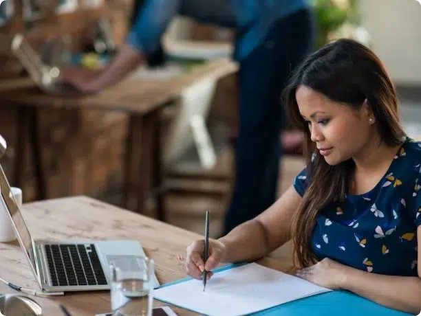 A woman sitting at a table, writing on a piece of paper